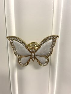 a white and gold butterfly brooch sitting on top of a door handle in front of a window