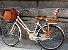 an old bicycle parked next to a stone wall with a brown leather bag on the seat