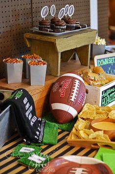 a football sitting on top of a table next to chips and cupcakes in paper cups