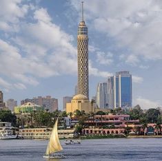 a sailboat in the water near a tall building with a spire on it's side