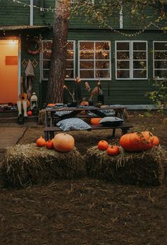 pumpkins and hay bales in front of a green house with lights strung from the windows