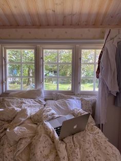 an open laptop computer sitting on top of a bed in front of two large windows