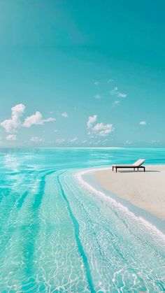 a bench sitting on top of a sandy beach next to the ocean under a blue sky