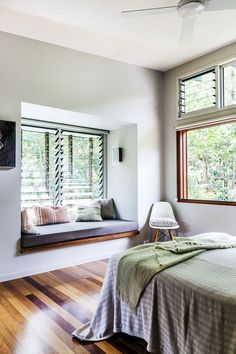 a bedroom with a bed, window seat and wooden floors in front of two windows