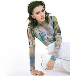 a woman with tattoos on her arms and legs crouching down in front of a white background