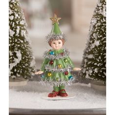 a small christmas tree with a little boy standing on it's side in front of snow covered trees