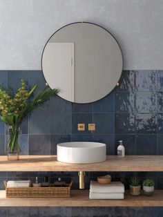 a round mirror on the wall above a sink in a bathroom with blue tiled walls