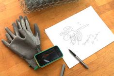 a pair of gloves sitting on top of a wooden floor next to a pen and paper