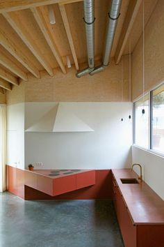 an empty room with red counter tops and exposed pipes in the ceiling, next to a large window