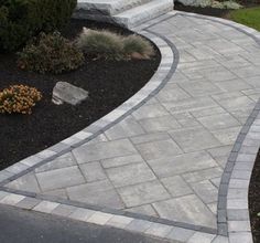 a brick walkway in the middle of a garden area next to bushes and flowers on either side