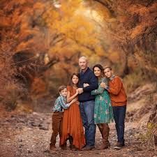 a family posing for a photo in the woods with fall foliage behind them and trees turning orange