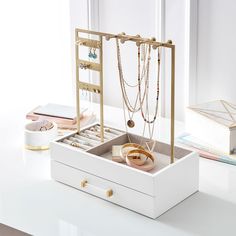 an open jewelry box sitting on top of a white counter next to a window with lots of necklaces hanging from it