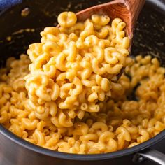 a wooden spoon full of macaroni and cheese in a pot with a blue towel