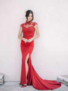 a woman in a red dress standing next to a white wall and posing for the camera