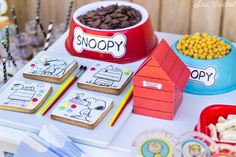 a table topped with lots of cookies and treats next to a bowl of dog food