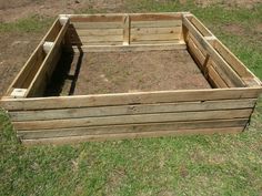 an empty wooden box sitting in the middle of some grass with no people around it