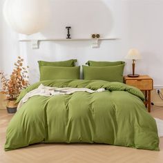 a bed with green sheets and pillows in a room next to a white light fixture