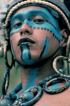 a man with blue paint on his face and body, wearing chains around his neck