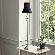 a lamp on a table next to a window with a potted plant in it