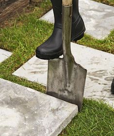 a pair of black boots and a shovel are on the grass near some stepping stones