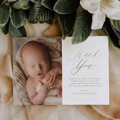 a baby is laying down on a blanket next to flowers and greenery with a thank you card