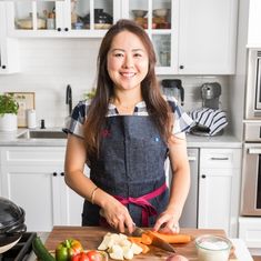 a woman in an apron cutting vegetables on a kitchen counter