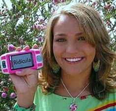 a woman holding up a pink and black electronic device with the words ridula written on it