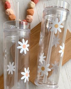 two clear tumblers with white daisies on them sitting next to a wooden tray