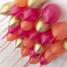 there are many pink and orange balloons on the wall with gold foiled stems attached to them