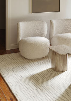 two white chairs sitting on top of a wooden floor next to a table in a living room