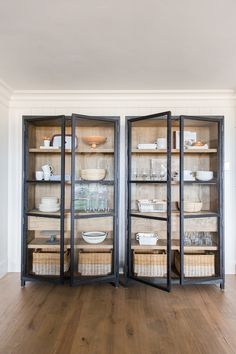 two open glass shelves with baskets and dishes in them on top of wooden flooring