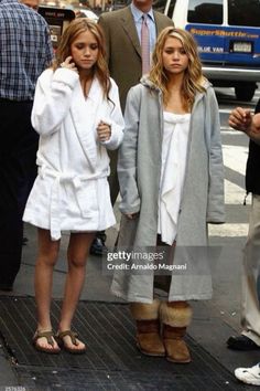 two women in bathrobes are walking down the street while one woman is talking on her cell phone