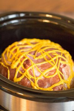 a crock pot filled with ham and cheese covered in melted yellow sauce on top of a wooden table