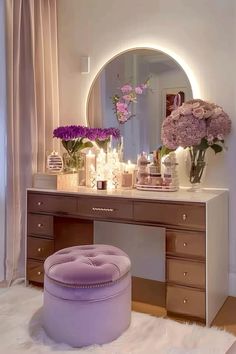 a vanity with flowers and candles on it in front of a round mirror above the counter