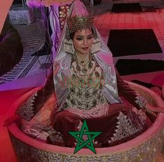 a woman dressed in an elaborately designed costume and headdress is sitting in a round container