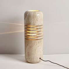 a white vase sitting on top of a table next to a light that is turned on