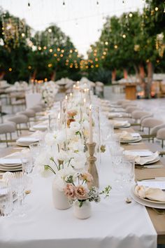 a long table with white and pink flowers on it is set for an outdoor dinner