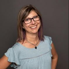 a woman wearing glasses standing in front of a gray wall