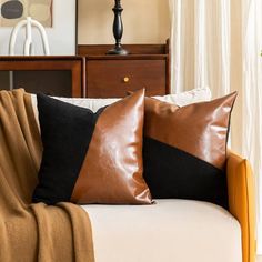 two brown and black pillows sitting on top of a white couch next to a lamp