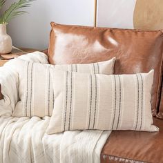 a brown leather couch with two pillows and a white blanket on top of it next to a potted plant