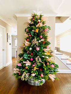 a decorated christmas tree in the middle of a living room with wooden floors and white walls