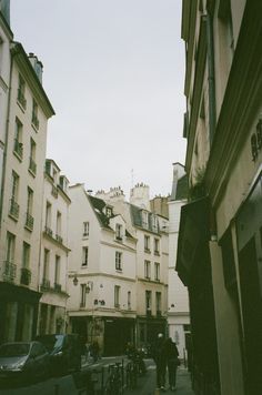 people are walking down the street in an old european city with tall buildings on either side