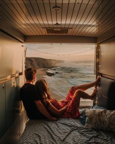 two people sitting on a bed looking out at the ocean