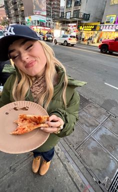 a woman holding a plate with a slice of pizza on it in front of a city street