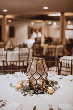 the table is set with white linens, candles and greenery for an elegant centerpiece