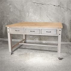 a white desk with two drawers and wheels on the bottom, in front of a concrete wall