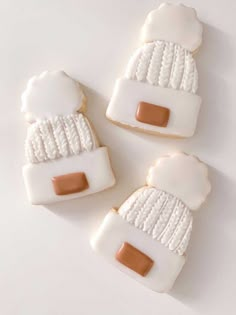 three decorated cookies with white frosting and brown icing, one in the shape of a hat