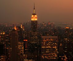 the empire building is lit up at night in new york city, ny as seen from top of the rock