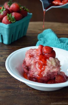 strawberries are being drizzled with syrup in a white bowl on a wooden table