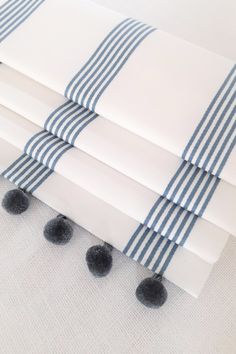 four white and blue striped napkins with black pom poms on them are laying next to each other